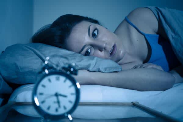 woman wide awake looking at alarm clock because of reasons you cant sleep